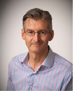 An image of Professor Alex Breeze wearing a lilac shirt and glasses