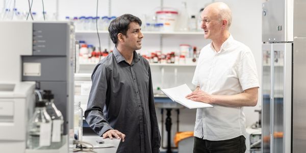 Two scientists standing talking to one another in front of lab equipment
