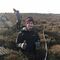 This image shows a man standing in a field of heather. There are two women in the background. They are all wearing coats, gloves and hats. The man is smiling and giving two thumbs up.