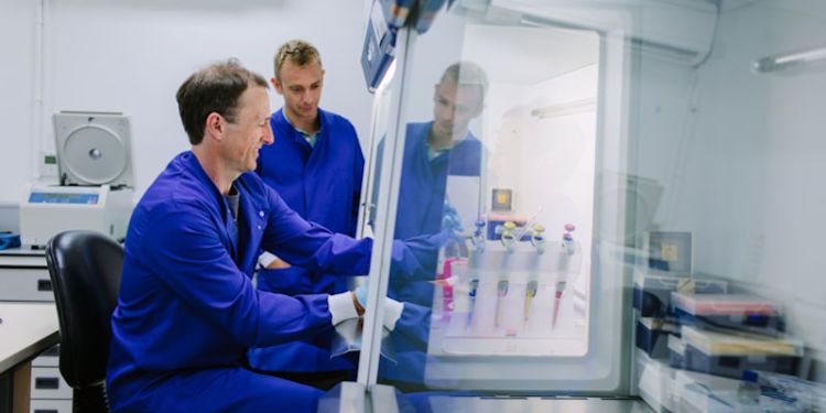 Two people working in a lab while wearing blue overalls.